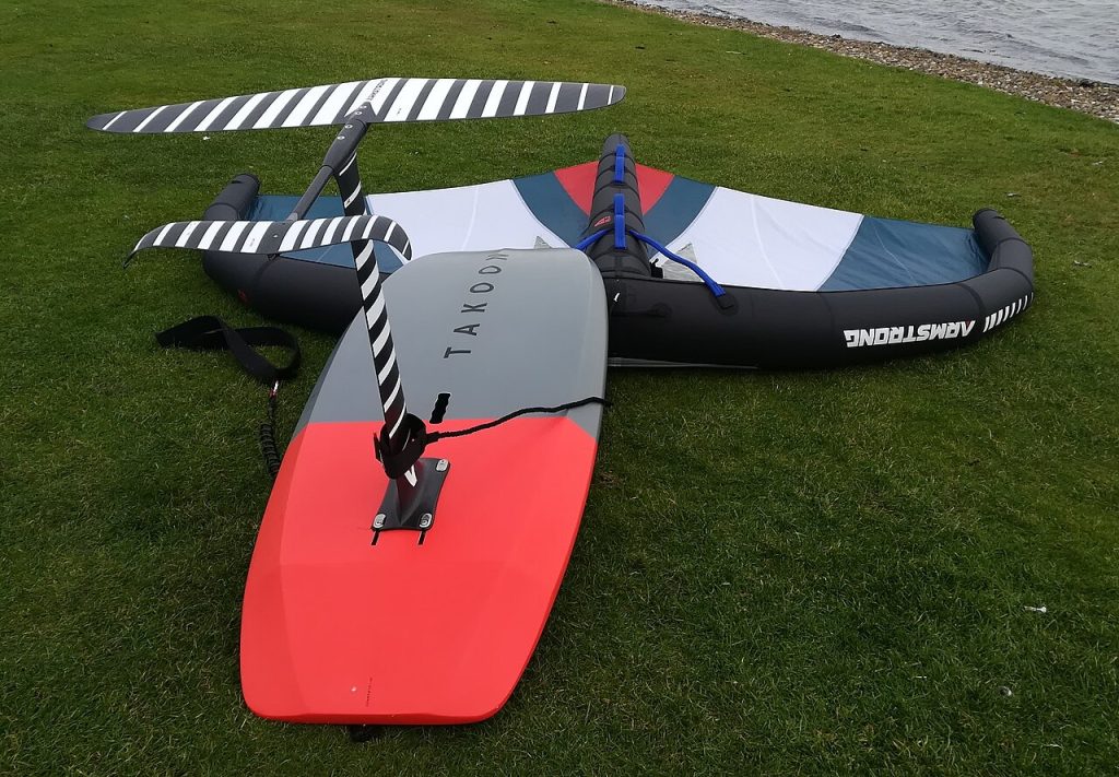 A wing foil set laid out on grass: inflatable wing, board and foil
